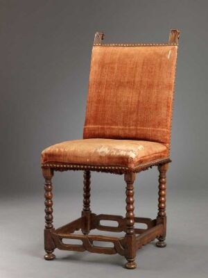  An antique wooden chair with turned stretchers and a tall, upholstered backrest in caramel color, depicted against a neutral grey background.