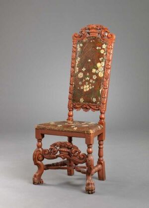  An antique-style wooden chair with intricate carvings and dark golden-brown upholstery embellished with lighter floral inlay designs, set against a plain gray background.