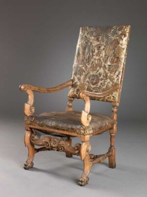  Antique wooden chair with detailed carvings and upholstered fabric in faded beige with a grayish-brown ornate pattern.