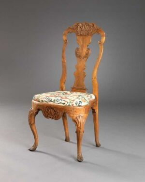 
 An antique wooden chair with elaborate carvings and a floral-patterned upholstered seat, against a light grey background.