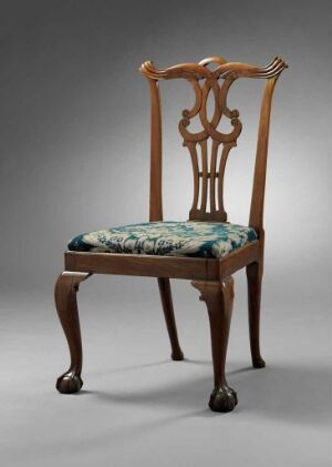  An antique-style wooden chair with a glossy, warm brown finish, featuring intricate fiddle-back design and floral upholstered seat in shades of green and blue.