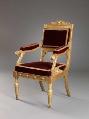  An ornate gilded armchair with a deep burgundy velvet upholstery set against a light grey background, reflecting a historical European style.