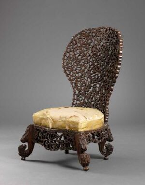  An ornate high-backed chair with a latticed dark brown back, plush golden-yellow cushioned seat, and intricately carved wooden legs against a neutral gray background. Artist name and title are unknown.