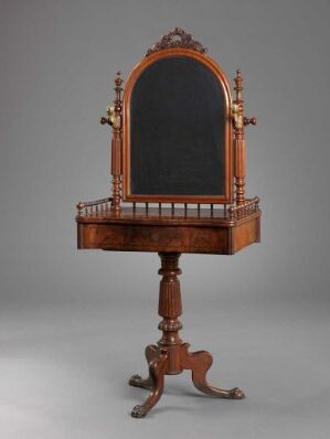  A vintage wooden dressing table with a central pedestal, claw-footed legs, and an ornamental frame, housing a mirror with an arched top and intricate carvings.