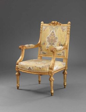  An antique gilded chair with a high back and armrests, upholstered in a cream fabric with a subtle floral pattern in soft beige, gold, and pastel tones, standing on a grey background.