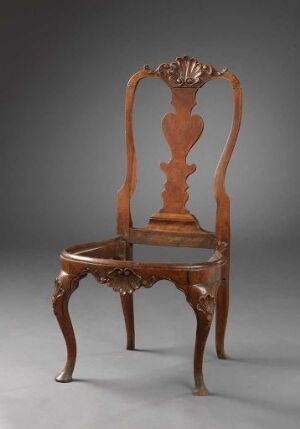  An antique wooden chair with elaborate carvings, featuring a shell-like design at the crest of the backrest and ornate floral motifs, with Cabriole-style legs. The chair is displayed against a plain gray background, highlighting its polished brown surface and artful craftsmanship.