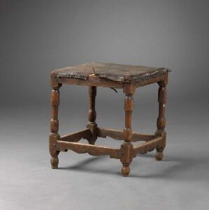  Antique wooden table with turned legs and stretchers, displaying a rich, brown patina set against a neutral gray background.