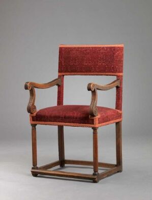  An antique wooden chair titled "Stol" by an unidentified artist, featuring a walnut frame with carved details, upholstered with red velvet showcasing carved patterns, and adorned with wool trim. It displays a combination of red and medium brown tones and exemplifies classic furniture design.