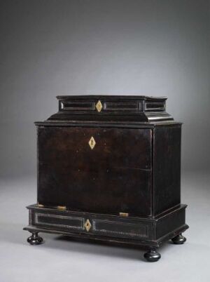  An antique dark wood chest with brass hardware, standing on a low base, against a neutral gray background.