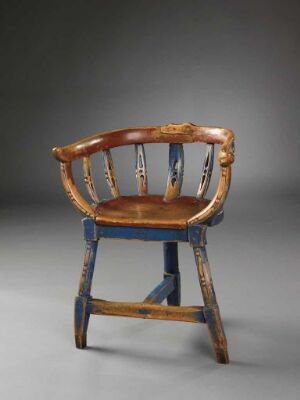  A traditional wooden captain's chair with a warm honey-tone curved armrest that doubles as a crest rail, and legs showing signs of wear. The chair features three vertical, cream-colored spindles on the backrest and a polished, contoured seat in dark and light brown hues. It has distinctive deep blue horizontal stretchers below the seat against a light-to-dark gray gradient background.