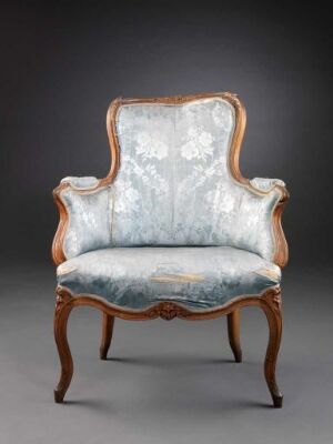  An antique armchair with curvaceous wooden frame in reddish-brown and plush pale blue upholstery with floral embroidery, set against a neutral gray background.