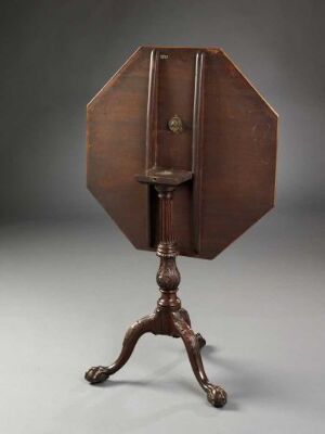  Antique octagonal wooden table with the top folded upwards on a tripod base with curved legs and clawed feet; the reddish-brown patina suggests aged hardwood.