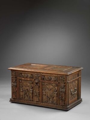  An intricately carved antique wooden chest with rich brown tones and detailed scenes in relief on the front and sides, displayed against a gradient gray background.