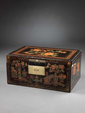  An antique lacquered wooden box with intricate floral and fruit inlays in yellow, orange, red, and green on the lid, surrounded by a geometric border. The sides feature similar floral patterns and there is a prominent keyhole plate on the front. The box is set against a dark gray background. Artistname and title are unknown.