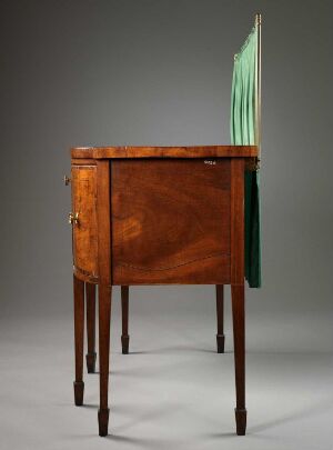  An antique wooden music cabinet with a closed door and a single brass knob, featuring an extendable section of seafoam green glass panes for holding sheet music, standing against a neutral dark gray background.