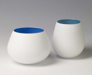  Two matte white glass bowls by Trine Drivsholm titled "Farvede skåler," exhibiting a modern design with vibrant cobalt and aqua blue interiors visible against a neutral background. The technique is blown colored glass with a matted white overlay.