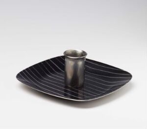  A modernist stainless steel serving dish with dark enamel finishing and radial grooved patterns by Grete Prytz Kittelsen, featuring a small cylindrical container centered on its triangular body.