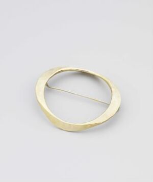  "Speil" by Tone Vigeland - A minimalistic oval-shaped silver jewelry piece with a matte finish, crafted by forging technique, displayed against a plain gray background.