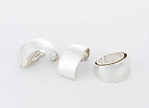  A set of three silver jewelry pieces by Tone Vigeland titled "Plain", consisting of a cuff bracelet and two rings with a polished, minimalist design, displayed on a white background.