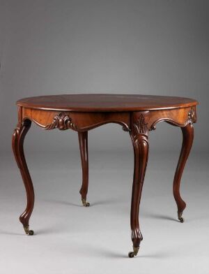  An antique-style wooden table with a glossy, oval top featuring raised edges, standing on four curvaceous legs with carved details and two discreet drawers with brass pull handles, on a simple gray background.