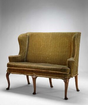  A vintage high-back golden olive velvet sofa with curving armrests and wooden tapered legs, set against a grey background.