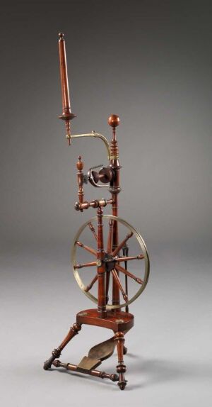  An elaborate mechanical apparatus with brass or copper components, including gears and tubing, on a wood-like tripod base, featuring a large horizontal wheel and smaller vertical one connected by a belt, with a glass element capturing light near the top, against a neutral gray background. Artist name and title are unknown.