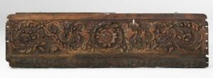  An antique wooden panel with detailed floral and foliate carving in a dark brown tone, exhibiting intricate craftsmanship and symmetrical patterns, with a prominent central medallion design.