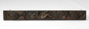  A long, dark brown carved wooden panel with intricate floral and scrollwork patterns displayed against a light, neutral background.