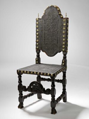  An antique high-backed wooden chair with decorative carvings and brass stud details on the back and seat edges, set against a light gray background.