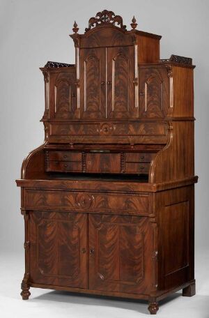  An antique wooden bureau bookcase with intricate designs and a slanted fold-down writing surface. The deep brown mahogany or walnut finish accentuates the carved details and the furniture's overall craftsmanship.