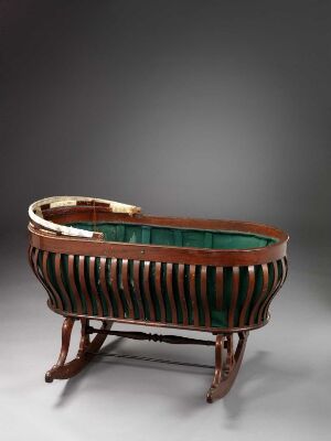  Antique wooden cradle with vertical dark brown slats and deep emerald green lining, resting on curved legs, with a neutral gray background. Artistname and title are unknown.