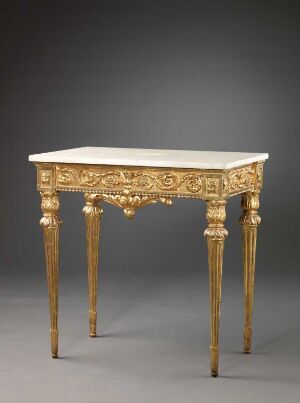  An antique-style gilded table with a rectangular top and intricately carved legs and apron, set against a plain grey background.