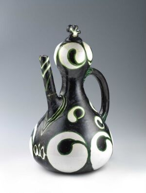  An artistic ceramic jug with a glossy black base featuring white swirl patterns with green accents and a stylized handle and spout, against a soft gray background. Artist name and title are unknown.