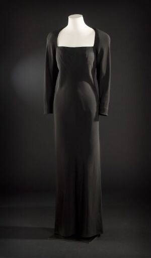  An elegant, full-length dress with long sleeves and a scoop neckline displayed on a mannequin against a dark, fading background. The dress appears to be made of a smooth, dark, possibly satin-like fabric that captures subtle highlights.