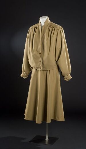  A vintage-style women's khaki dress with a cowl neckline and long puffed sleeves on a mannequin against a dark background. The dress has a cinched waist and a mid-calf length skirt, creating an elegant silhouette.