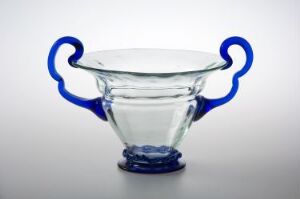  A clear glass bowl with cobalt blue handles on a white to grey gradient background.