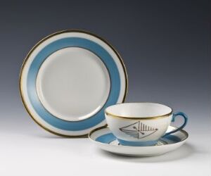  A porcelain tea set with a round plate in the back displaying blue and gold edges and a white center; a cup with a geometric design and gold rim sits on a matching saucer with concentric blue and gold circles, all against a grey background.