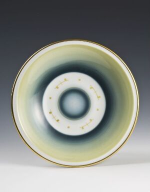  A porcelain deep plate titled "Modell 2057" by Porsgrunds Porselænsfabrik AS displaying a color gradient from ivory to pale yellow, pastel green, and slate blue towards the center, with gold rim accents and a ring of gold dots in the middle.