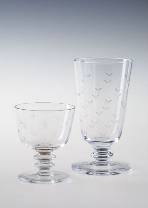  Two pieces of fine, clear blown glass with engraved decor, titled "Ely" by artist Ståle Kyllingstad, consisting of a short, wide bowl on the left and a tall drinking glass on the right, both with subtle engraved plant-like patterns, set against a soft gradient background that transitions from light at the top to dark at the bottom.