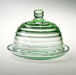  A decorative press glass object designed by Sverre Pettersen, with a transparent green color. It features concentric circular ridges and consists of a dome-shaped lid with a small knob handle, fitting onto a shallow dish base with a flat rim.