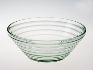  A translucent seafoam green glass bowl with concentric circles, designed by Willy Johansson; displayed against a neutral background. The bowl's simple and elegant design reflects the soft light, enhancing its delicate color and shapely form.