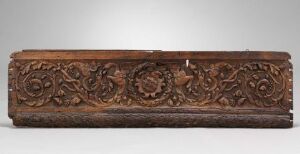  An antique wooden beam with intricate floral and spiral carvings, rendered in rich brown tones against a neutral gray background.