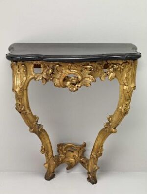  An ornate, Baroque-style table with a dark tabletop and a gilded body featuring elaborate scrollwork and acanthus leaf motifs. The table's legs are curved and ornate, standing against a plain, light-colored background.