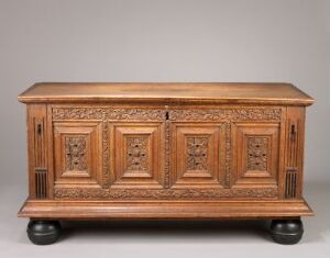  An intricately carved wooden chest with decorative panels, showing detailed geometrical patterns on a rich, reddish-brown hardwood surface, standing on rounded feet.