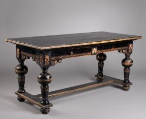  An antique dark wood table with turned legs and intricate geometric openwork carving beneath the top, set against a soft grey background.