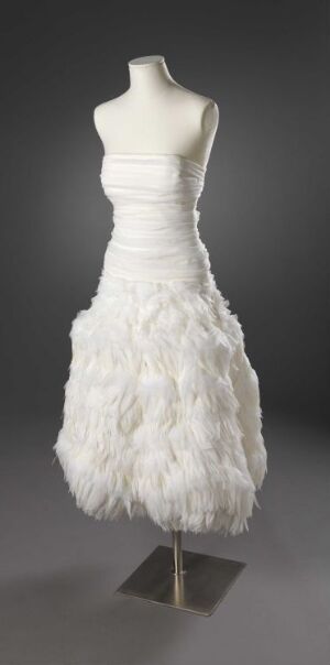  A strapless white dress with a ribbed bodice and feathered skirt on a headless and armless mannequin against a gray background.