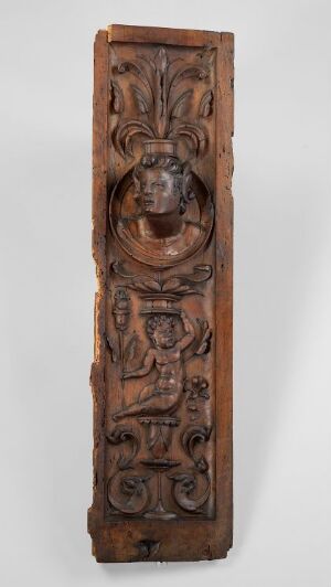  A vertical, dark brown, wooden panel with intricate carvings, including a central female figure's face, stylized botanical motifs at the top, and classical scrollwork below, on a light gray background. Artist name and title are unknown.