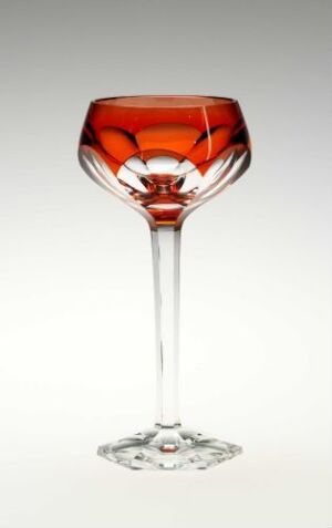  An elegant, clear glass with a long stem and an angular bowl filled with an amber or reddish-brown liquid against a light background.