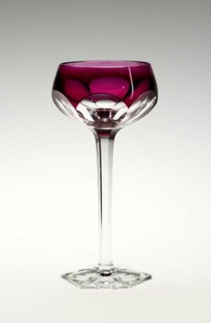  An elegant glass goblet with a rich magenta-colored bowl, clear stem, and round base, standing against a light grey background.