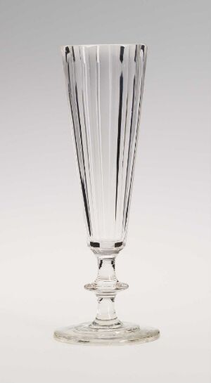  A tall, clear fluted glass goblet with an elongated bowl and a simple, smooth stem and foot, standing against a light background.